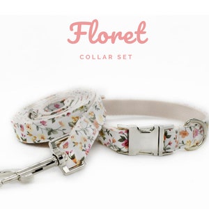 K&ouml;nnte beinhalten: Ein floraler Halsband-Set mit einem wei&szlig;en Halsband und einer passenden Leine, verziert mit einem Muster aus kleinen rosa, gelben und orangefarbenen Blumen. Das Set enth&auml;lt eine silberfarbene Metallschnalle und einen Leinenverschluss. Der Text "Floret COLLAR SET" ist rosa.