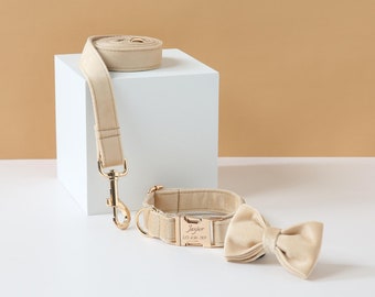 Könnte beinhalten: Ein beigefarbenes Hundehalsband und eine Leine mit einer goldenen Schnalle und einer Schleife. Das Halsband ist mit dem Namen "Jasper" und der Telefonnummer "123 456 789" graviert.