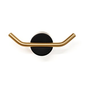 May include: A gold metal hook with a black circular base. The hook is curved and has a modern design.