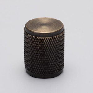 May include: A round, antique brass cabinet knob with a textured, diamond-shaped pattern. The knob has a smooth, polished top.