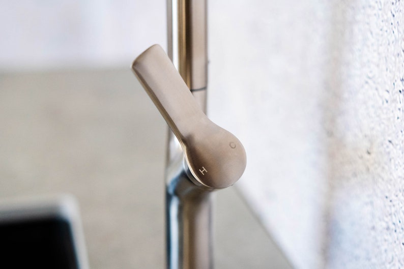 May include: Close-up of a silver faucet handle with the letters 'H' and 'C' engraved on the knob.