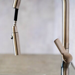 May include: A close-up of a silver kitchen faucet with a pull-down sprayer. The faucet has a single handle and a lever for switching between spray and stream.