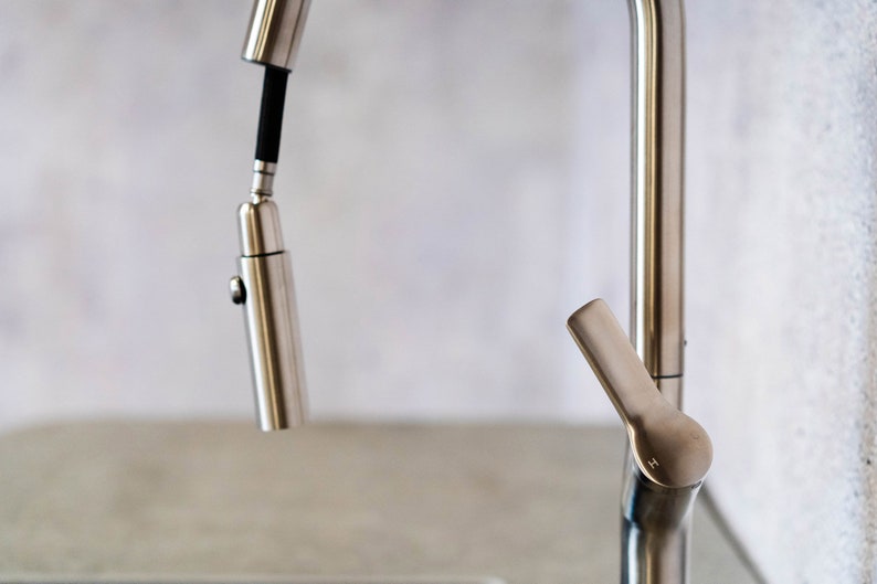 May include: A close-up of a silver kitchen faucet with a pull-down sprayer. The faucet has a single handle and a lever for switching between spray and stream.