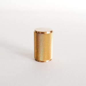 May include: A gold-coloured metal knob with a textured surface. The knob is cylindrical in shape.