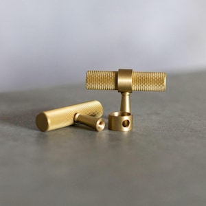 May include: Two gold metal cabinet knobs with a textured finish. The knobs are in the shape of a bar with a round base.