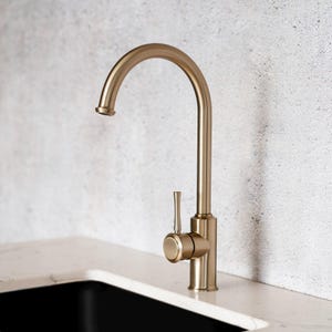 May include: A gold kitchen tap with a single lever handle. The tap has a high arc spout and a modern design.