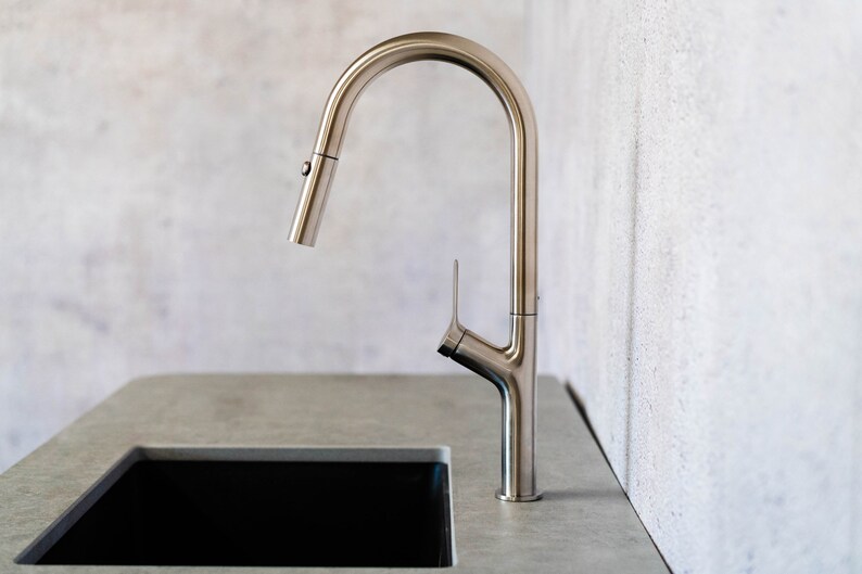 May include: A silver kitchen faucet with a high arc spout and a single lever handle. The faucet is mounted on a gray countertop.
