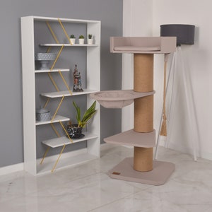 Peut inclure: Un arbre à chat moderne aux tons beige et marron. Il comprend un poteau à griffer en corde, plusieurs plateformes et un lit douillet. Une étagère blanche avec des accents jaunes et des objets décoratifs est également présente.