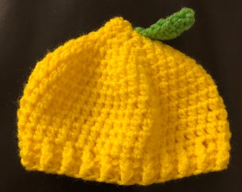 May include: A yellow crocheted lemon hat with a green stem.