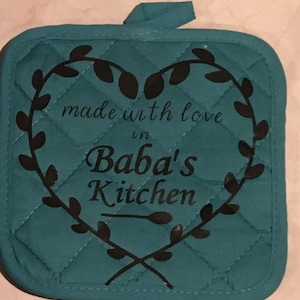 May include: Teal quilted pot holder with a black heart-shaped design. The heart features a wreath of leaves and the text "made with love in Baba's Kitchen".
