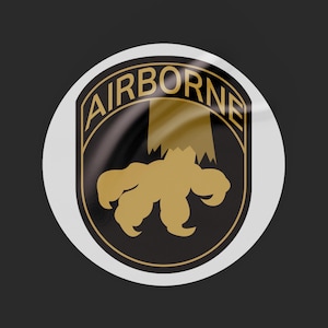 Op de afbeelding: Een witte ronde sticker met een zwart en gouden adelaar-klauw ontwerp. De tekst "AIRBORNE" is geschreven in een gouden boog rond de klauw.