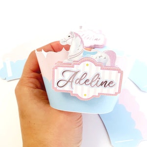 May include: A light blue and pink cupcake wrapper with a white horse and a sign that says "Adeline".