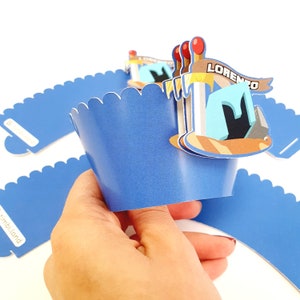 May include: Blue cupcake wrappers with a scalloped edge. A topper with a Minecraft-themed design features a pickaxe, a block of turquoise, and a banner that says "LORENZO".