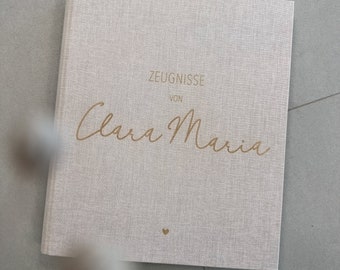 Può includere: Un album beige in lino con texture, con la scritta dorata "ZEUGNISSE VON Clara Maria" e un piccolo cuore dorato.