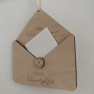 May include: A wooden envelope with a white card inside. The envelope has the text "Lieber Weihnachtsmann" and "EMILIAS Wunschzettel" on it. There is a round wooden seal with the text "North Pole Express Delivery" and a snowflake.