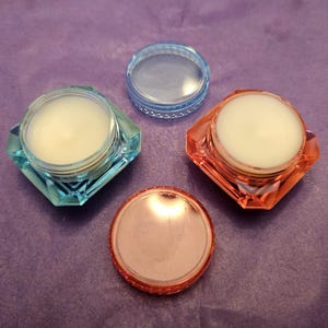 May include: Three small containers with lids. Two containers are light blue with a clear lid. One container is orange with a clear lid. The containers are filled with a white substance.