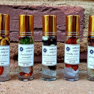 May include: Eight 10 ml roll-on bottles of essential oil blends with gold lids and labels. The labels feature a variety of winter-themed scents, including "rusted pine", "apple cider", "christmas wreath", "hot chocolate", "candy cane", "gingerbread man", "warm chai tea", and "warm chai tea".