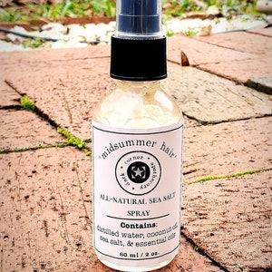 May include: A clear glass bottle with a black spray top and a white label that reads "midsummer hair corner apothecary" and "ALL-NATURAL SEA SALT SPRAY". The label also lists the ingredients: "distilled water, coconut oil, sea salt, & essential oils" and the size: "60 ml / 2 oz."