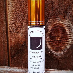 May include: A gold roll-on bottle with a black and white label that says "new moon intoxicating perfume with coconut oil & pure essential oils 10 ml."
