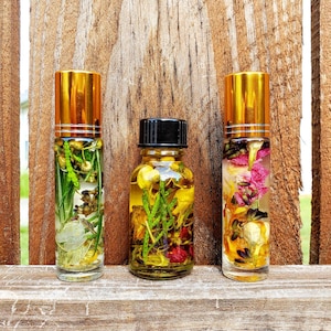 May include: Three glass bottles with gold lids filled with dried flowers and herbs. The bottles are on a wooden surface.