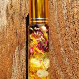 May include: A clear glass roller bottle with a gold lid filled with yellow, orange, pink, and purple dried flowers and herbs.