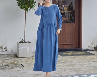 May include: A long, light blue, casual dress with long sleeves and a button-up front. The dress has a gathered waist and a relaxed fit. The model is wearing white sneakers.
