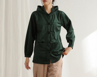 May include: A dark green hooded jacket with long sleeves and a button-up front. The jacket features two front pockets and a relaxed fit. The fabric looks soft and textured. The model is wearing tan trousers.