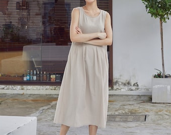 May include: A sleeveless, beige linen dress with a pleated skirt. The dress is knee-length and has a relaxed fit.