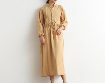 May include: A long-sleeved, light brown dress with a button-up front and a tie at the waist. The dress has a relaxed fit and is made of a soft, comfortable fabric.