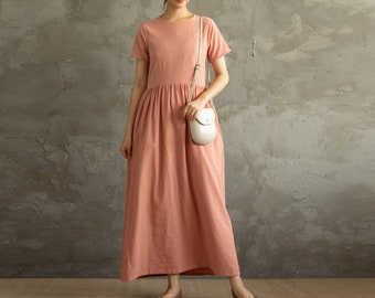 May include: A woman wearing a pink, short-sleeved, maxi dress with a white crossbody bag.