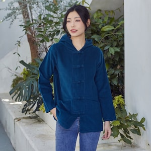 Puede incluir: Una chaqueta azul turquesa con capucha, cierre de botones y corte holgado. La chaqueta tiene un estilo chino tradicional con cuello alto y silueta suelta.