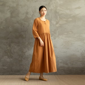 May include: A long, loose-fitting, rust-colored dress with a round neckline and three-quarter sleeves. The dress has a gathered waist and a simple, casual style.