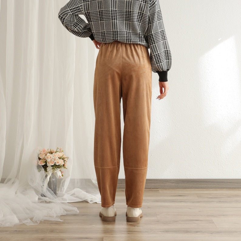 Puede incluir: Una persona con una camisa de manga larga a cuadros blancos y negros y pantalones de pana marrones. Los pantalones son de cintura alta y pernera ancha. La persona tambi&eacute;n lleva zapatos blancos.