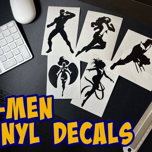 May include: Five black vinyl decals featuring silhouettes of X-Men characters: Wolverine, Storm, Cyclops, Rogue, and Jean Grey. The decals are on white paper and the text "X-MEN VINYL DECALS" is in yellow letters on a blue background.