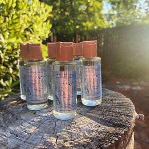 May include: Five small clear glass bottles with brown caps, each containing a liquid. The bottles are labelled "MIDNIGHT SERENITY" with a crescent moon and star design. The bottles are arranged on a wooden surface.