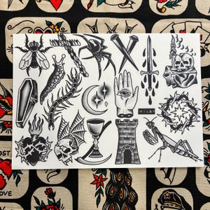 Puede incluir: Hoja de flash de tatuaje en blanco y negro con varios diseños de tatuajes tradicionales. Incluye una mosca, una araña, un ataúd, una cruz, una daga, una calavera, una mano con un ojo y otros símbolos góticos. El nombre del artista, WILBY, está impreso.