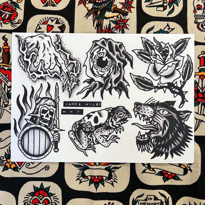 May include: Black and white tattoo flash sheet featuring traditional designs. Includes a hand, an eye, a rose, a skeleton warrior, a frog, and a snarling wolf. The artist's name, James Wilby, is printed on the sheet.