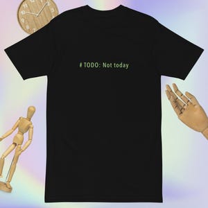 May include: Black t-shirt with the text "# TODO: Not today" in green. The shirt is shown against a light background, with a wooden clock and a wooden hand model.
