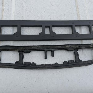 May include: Two black rectangular rubber components with cut-out sections. The top piece is a solid, newer-looking rectangle. The bottom piece is a similar shape, but appears older and more worn, with a textured surface.