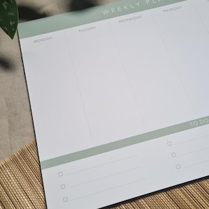 Op de afbeelding: Een weekplanner met een groene kop en een wit lichaam. De kop heeft de tekst "WEEKLY PLANNER" en de dagen van de week staan eronder vermeld: Maandag, Dinsdag, Woensdag, Donderdag, Vrijdag, Zaterdag en Zondag. Het lichaam van de planner heeft lijnen om taken op te schrijven en een "TO DO"-sectie met vinkjes.