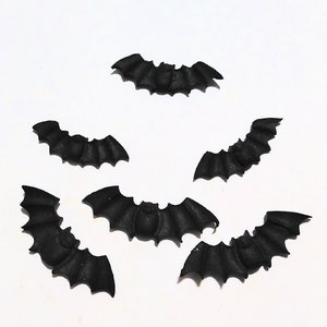 May include: Six black paper bats, each with a slightly different shape and size, are scattered on a white background. The bats are a popular Halloween decoration.