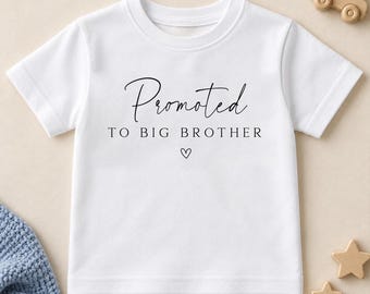 Może przedstawiać: Biała koszulka z krótkim rękawem z czarnym nadrukiem Promoted TO BIG BROTHER oraz małym symbolem serca umieszczonym pod napisem. Koszulka posiada klasyczny okrągły dekolt oraz proste wykończenie dołu w minimalistycznym stylu.