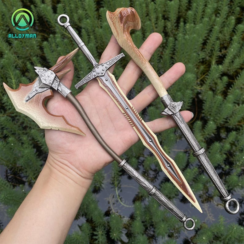 Puede incluir: Cuatro armas de fantas&iacute;a en miniatura: un hacha plateada con una hoja beige, una espada plateada con una hoja marr&oacute;n, una espada plateada con un mango de hueso y un garrote plateado con un mango de hueso. Las armas se sostienen sobre un fondo de follaje verde.