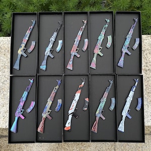 May include: Ten decorative AK-47 style rifles with colorful, patterned designs. Each rifle is displayed in a black box with a matching magazine. The rifles feature various color schemes, including blue, red, and green, with intricate patterns.