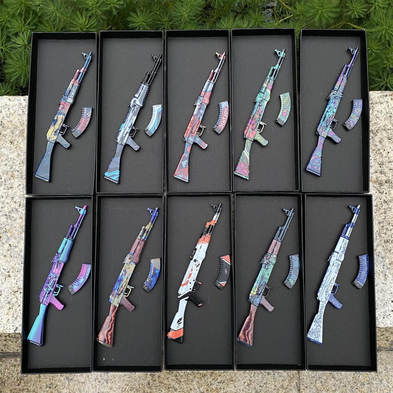 May include: Ten decorative AK-47 style rifles with colorful, patterned designs. Each rifle is displayed in a black box with a matching magazine. The rifles feature various color schemes, including blue, red, and green, with intricate patterns.