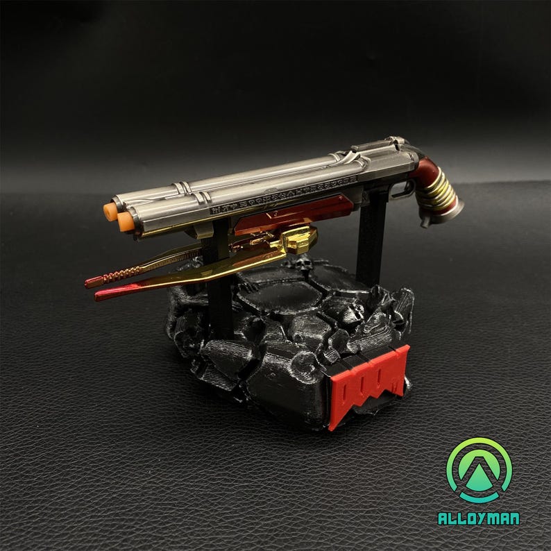Pu&ograve; includere: Una replica in metallo argentato e rosso di un fucile a doppia canna con un grilletto dorato e un supporto nero con la parola "DOOM" stampata in rosso.