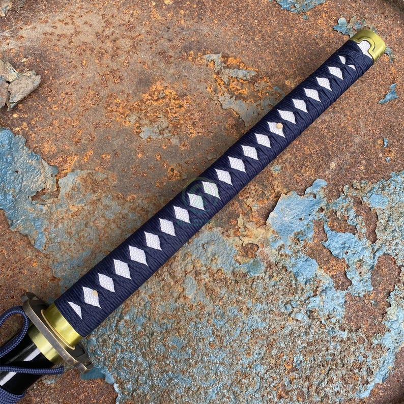 Może przedstawiać: Miecz katana z granatowym uchwytem owiniętym we wz&oacute;r romb&oacute;w z białymi akcentami. Ochraniacz miecza jest złoty, a ostrze czarne. Miecz jest umieszczony na zardzewiałym, teksturowanym tle.