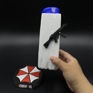 May include: A blue beret with a badge, a white rectangular object with a black gun attached, and a black round object with a red and white umbrella design and the text "RESIDENT EVIL".