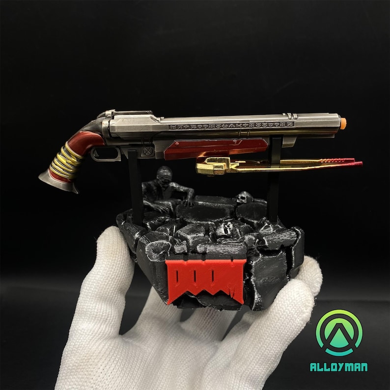 Pu&ograve; includere: Una replica in metallo nero e rosso del fucile a pompa del Doom Slayer del videogioco Doom Eternal. Il fucile &egrave; esposto su una base di roccia nera e grigia con il logo Doom. La base &egrave; su una superficie bianca.