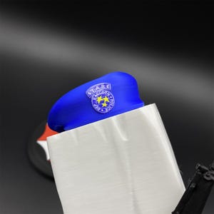 May include: A blue beret with a circular patch featuring the text "S.T.A.R.S. Raccoon Police Dept" and two yellow stars. The beret is partially obscured by a white object, with a black background.